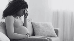 Pregnant woman sat on a sofa holding her head in her hands and looking unwell