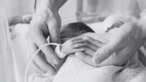 Newborn baby in a hospital incubator with a parent's hands.